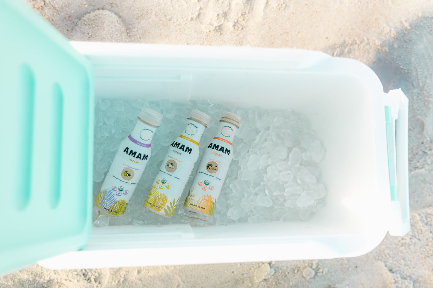 Three bottles labeled 'MAMA' in a cooler on sand