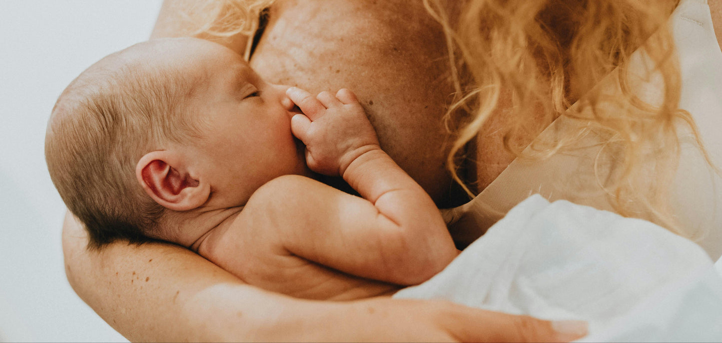 Newborn baby being held by a person with long hair against a neutral background