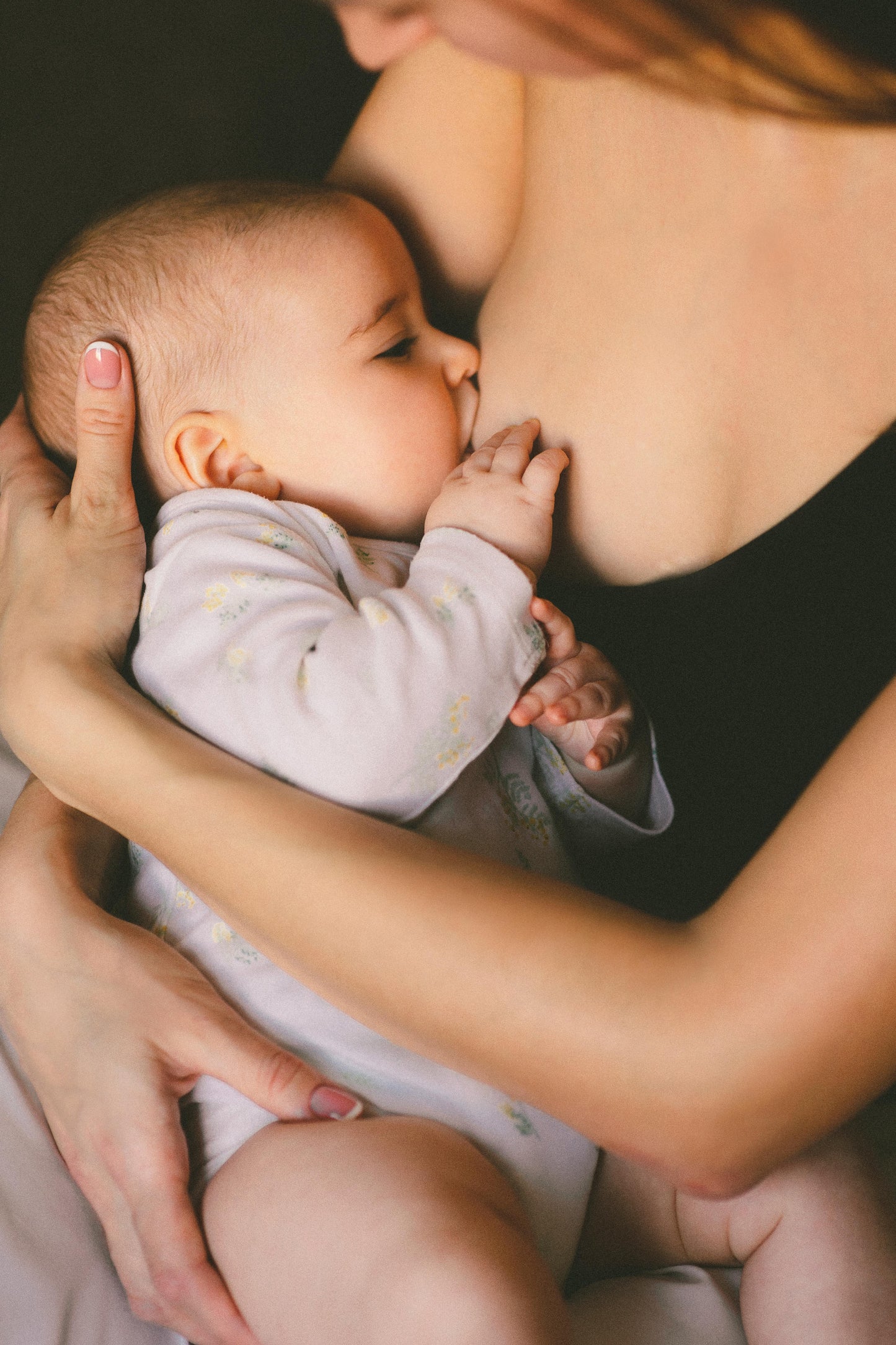 Baby being breastfed by a woman with a dark background