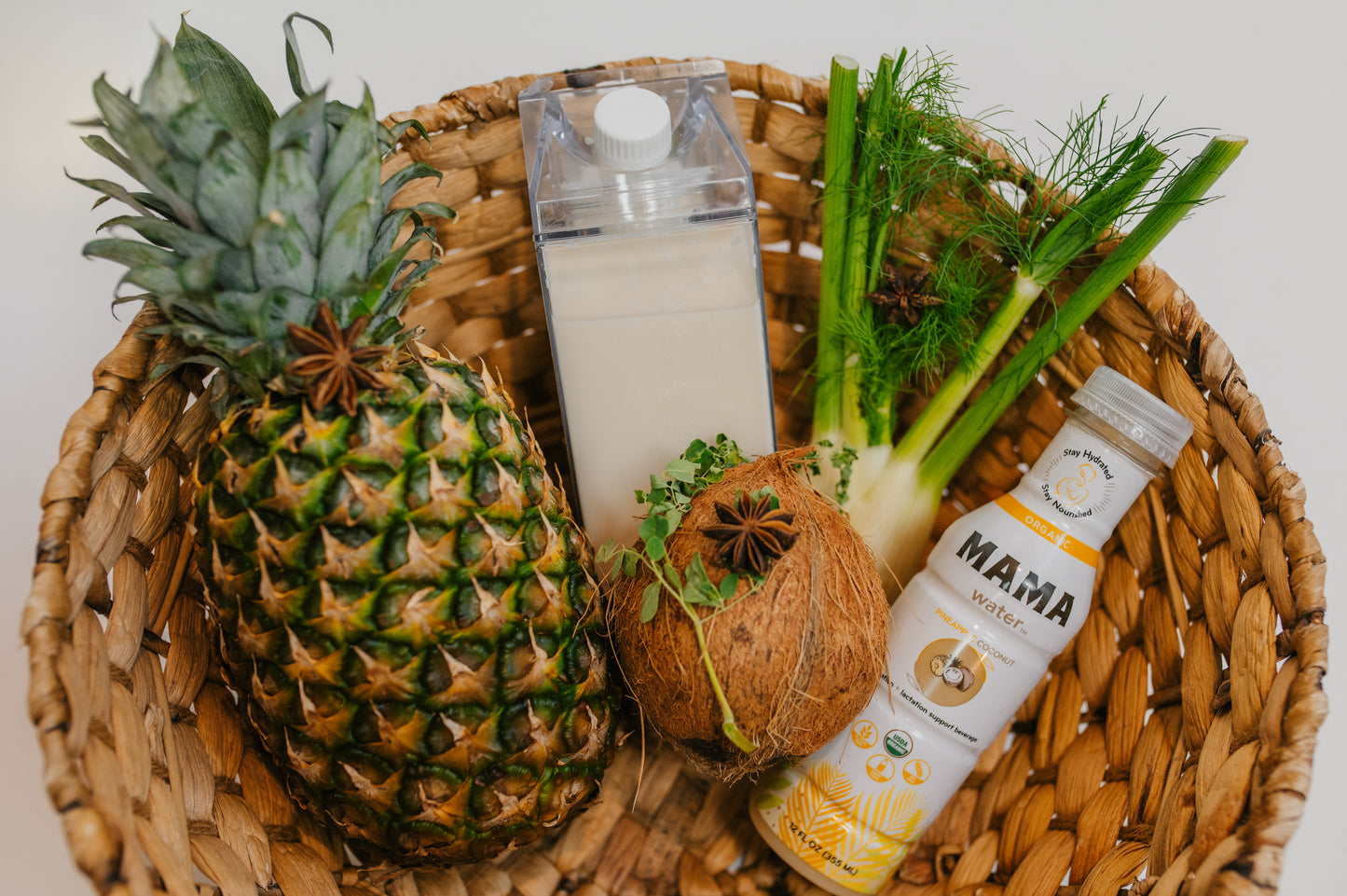 Pineapple, coconut, and bottles on a woven tray with a white background